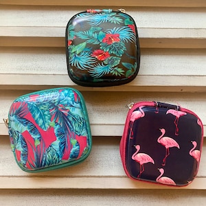 Peut inclure: Trois petites pochettes zipp&eacute;es avec diff&eacute;rents imprim&eacute;s tropicaux. La premi&egrave;re pochette a un fond vert fonc&eacute; avec des feuilles et des fleurs tropicales rouges et vertes. La deuxi&egrave;me pochette a un fond rose avec des feuilles tropicales vertes et bleues. La troisi&egrave;me pochette a un fond bleu fonc&eacute; avec des flamants roses.