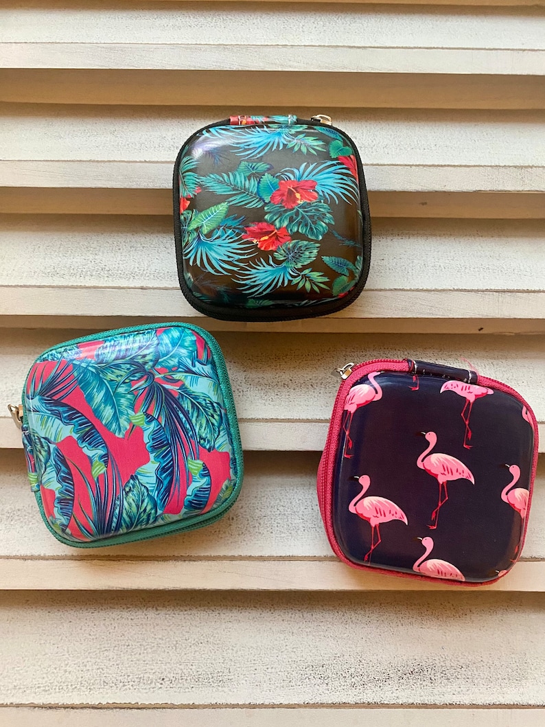 Peut inclure: Trois petites pochettes zipp&eacute;es avec diff&eacute;rents imprim&eacute;s tropicaux. La premi&egrave;re pochette a un fond vert fonc&eacute; avec des feuilles et des fleurs tropicales rouges et vertes. La deuxi&egrave;me pochette a un fond rose avec des feuilles tropicales vertes et bleues. La troisi&egrave;me pochette a un fond bleu fonc&eacute; avec des flamants roses.