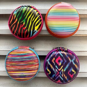 May include: Four round zippered cases with vibrant designs. One features a rainbow zebra print, another has horizontal rainbow stripes, a third has colorful horizontal lines, and the last has a geometric pattern in purple and pink.