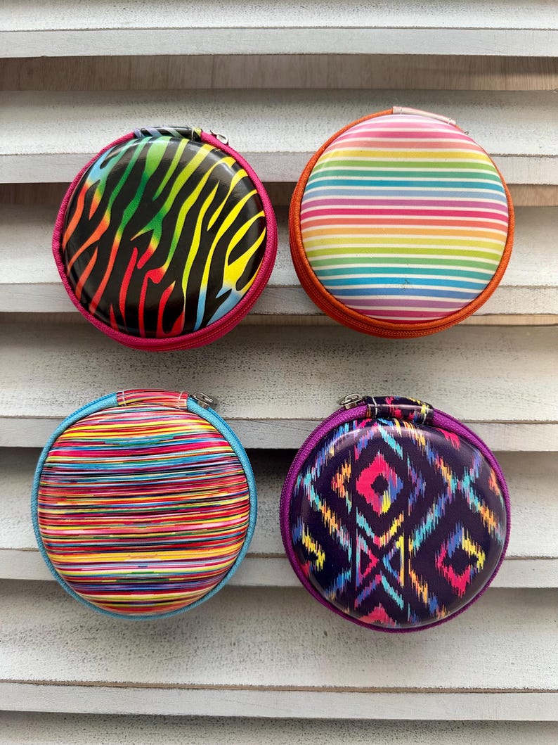 May include: Four round zippered cases with vibrant designs. One features a rainbow zebra print, another has horizontal rainbow stripes, a third has colorful horizontal lines, and the last has a geometric pattern in purple and pink.