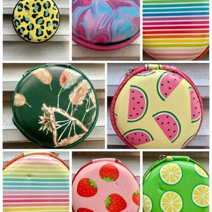May include: Collection of round, zippered cases with various designs. Includes a yellow case with black leopard spots, a pink and blue swirled case, and a case with rainbow stripes. Other cases feature watermelon slices, strawberries, and lemon slices.