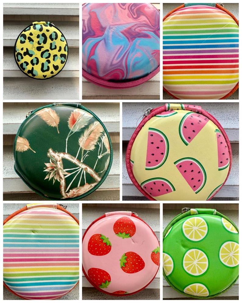 May include: Collection of round, zippered cases with various designs. Includes a yellow case with black leopard spots, a pink and blue swirled case, and a case with rainbow stripes. Other cases feature watermelon slices, strawberries, and lemon slices.