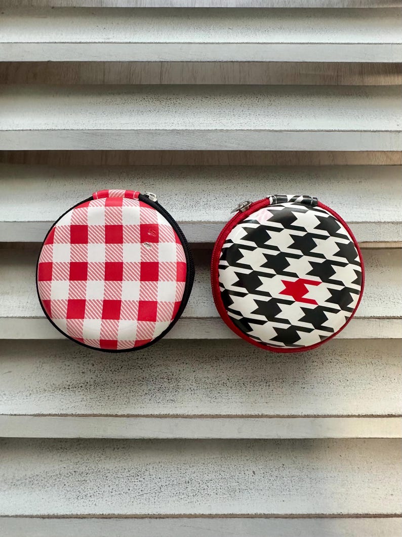 May include: Two round zippered cases. One case has a red and white gingham pattern, the other has a black and white houndstooth pattern with a red accent. Both cases have black trim and silver zippers.