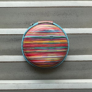 Peut inclure: Une pochette ovale de couleur ray&eacute;e avec une bordure bleue. Le sac a une fermeture &eacute;clair et une petite poign&eacute;e.