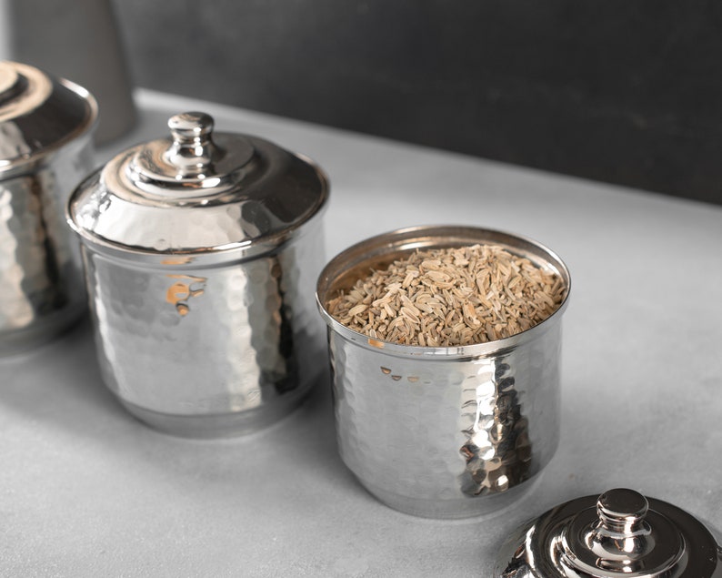 May include: Three silver hammered metal containers with lids. One container is filled with dried fennel seeds.