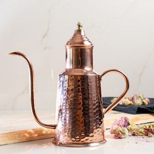 May include: A hammered copper oil or vinegar dispenser with a spout and a lid. The dispenser has a rustic, antique look.