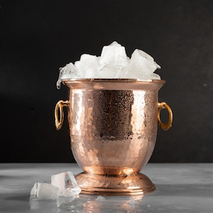 May include: A hammered copper ice bucket with gold-tone handles filled with ice cubes.
