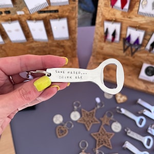 May include: A silver bottle opener keychain with the text "Save Water... Drink Ale".