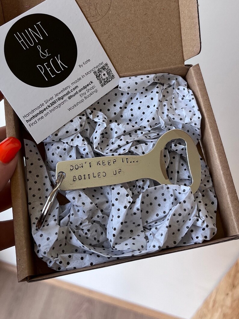 May include: A silver bottle opener keychain with the text "DON'T KEEP IT... BOTTLED UP" engraved on it. The keychain is in a small box with white tissue paper.