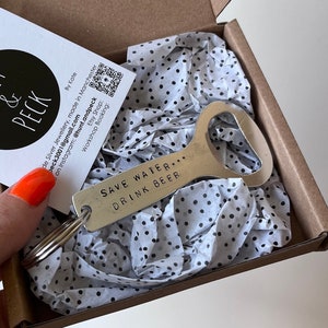 May include: A silver bottle opener with a black keychain ring. The bottle opener has the text "Save Water... Drink Beer" engraved on it.