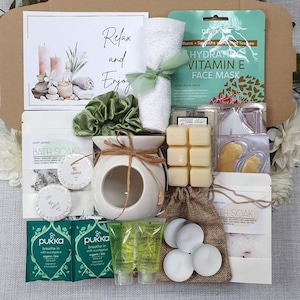 May include: A gift box filled with self-care items. Includes a white ceramic oil diffuser, bath soak, face mask, candles, and other relaxation products. The box also contains a card with the words "Relax and Enjoy".