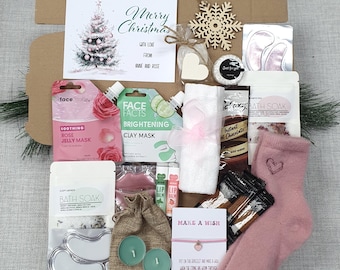 May include: A Christmas gift box filled with self-care items. Includes a card that says "Merry Christmas", face masks, bath soak, candles, socks, a bracelet, and a small towel. The box is brown and contains a variety of pink and white items.