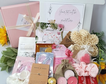 May include: A pink gift box filled with self-care items, including bath products, candles, and a bracelet. The box contains a variety of pink and white items, such as bath salts, lip masks, and scrunchies. The text "Your text will be printed here" is visible on a card.