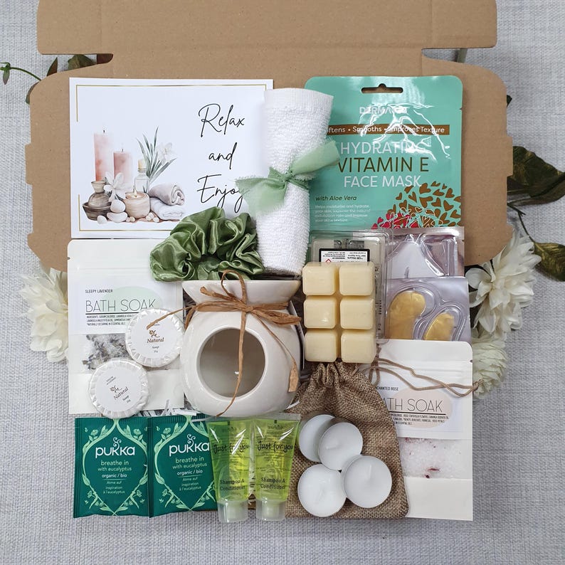 May include: A gift box filled with self-care items. Includes a white ceramic oil diffuser, bath soak, face mask, candles, and other relaxation products. The box also contains a card with the words "Relax and Enjoy".