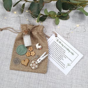 May include: A hessian bag containing wedding favours: a small glass jar, wooden embellishments, a key charm, and a decorative pin. A tag reads "The little bag of wedding wishes."