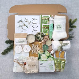 Może przedstawiać: Brązowe pudełko prezentowe wypełnione artykułami do pielęgnacji. Zawiera kartkę z napisem "From Your Secret Santa", sól do kąpieli, świece, maseczkę do twarzy, herbatę, ręcznik i inne produkty spa. Przedmioty są ułożone w pudełku.