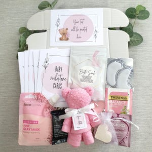 May include: A pink and white baby shower gift box with a pink teddy bear, bath soak, tea, face mask, and other self-care items. The box includes a card that says "Your text will be printed here".