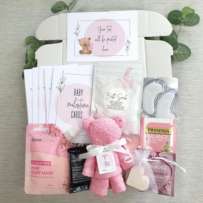 May include: A pink and white baby shower gift box with a pink teddy bear, bath soak, tea, face mask, and other self-care items. The box includes a card that says "Your text will be printed here".