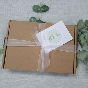 May include: A brown cardboard gift box tied with a sheer white ribbon. A white tag with the words "gift for You" in script is attached to the ribbon. The tag has a light green circle and floral accents.