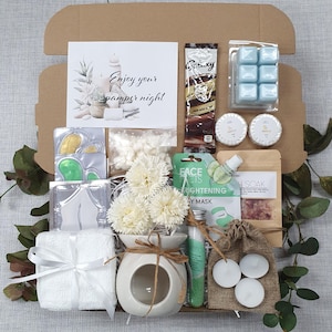 May include: A gift box filled with pampering items. Includes a card with text "Enjoy your pamper night", a chocolate bar, blue wax melts, soaps, eye masks, a diffuser with flowers, a face mask, bath soak, tea lights, and a small towel.