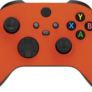 May include: A vibrant orange wireless video game controller featuring two black analog sticks, a black directional pad, and four action buttons labeled Y, X, B, and A in yellow, blue, red, and green. It includes central menu, share, and view buttons.