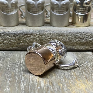 May include: A silver and copper figurine of a cartoon character with a wide grin and outstretched arms. The character is wearing a copper hat and has a copper body.
