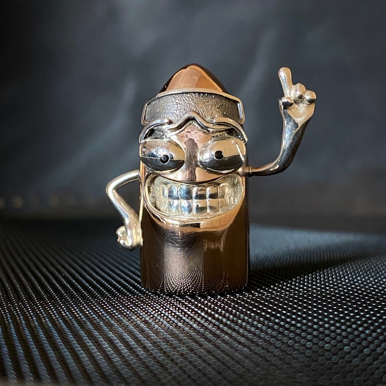 May include: A silver and gold figurine of a cartoon character with a toothy grin, wearing a silver headband and raising one arm in the air.