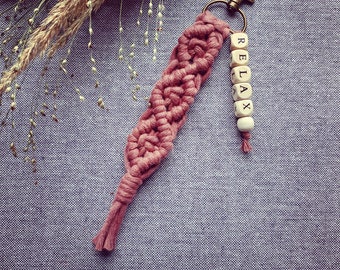 May include: A pink macrame keychain with a wooden bead charm that spells "RELAX".