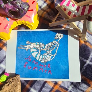 May include: A blue and white striped life preserver with a skeleton sitting on it. The skeleton is wearing a blue and white striped shirt. The background is blue and the text "Summer Summer" is written in pink.