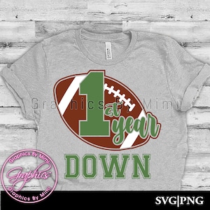 May include: A grey t-shirt with a green number one and the words "1st year down" on a brown and white football graphic.