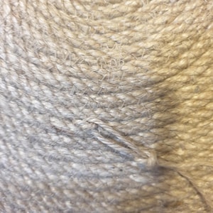 May include: Close-up of a natural fiber rope, woven in a spiral pattern. The rope is a light beige color and has a rough texture.