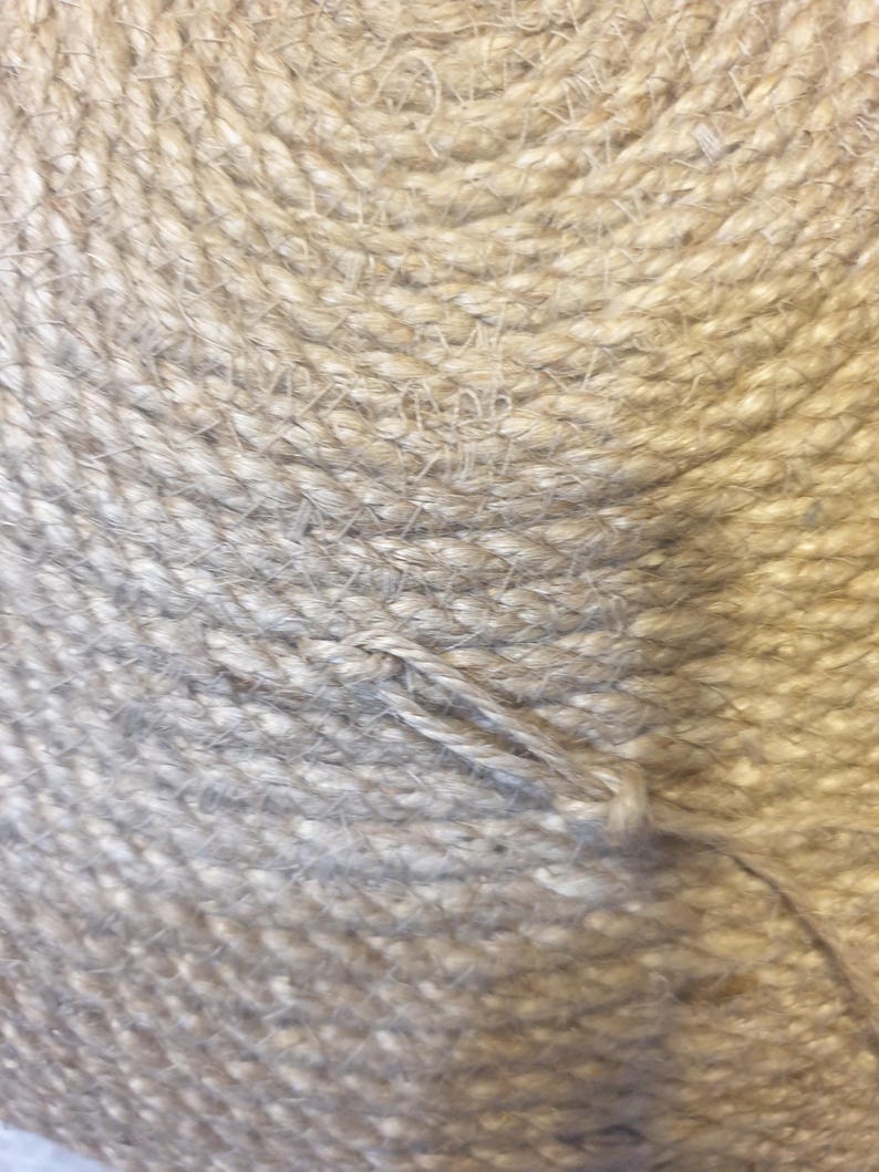 May include: Close-up of a natural fiber rope, woven in a spiral pattern. The rope is a light beige color and has a rough texture.