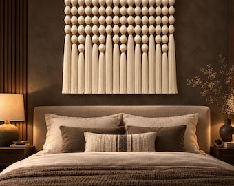 May include: A wall hanging featuring a grid of cream-colored wooden spheres suspended from a horizontal rod. The bottom edge of the piece is finished with a series of long, vertical cream-colored fabric tassels of varying lengths.