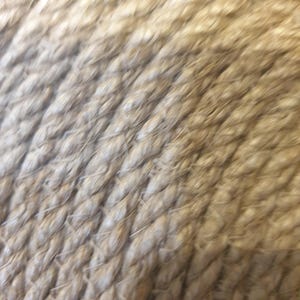 May include: Close-up of a natural fiber rope, showing the texture and weave of the fibers. The rope is a light brown color and has a rough, textured surface.