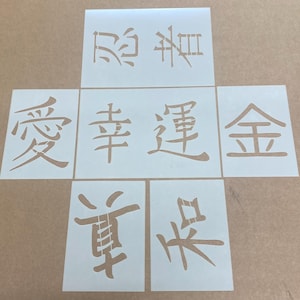 以下が含まれることがあります： 黒い輪郭の日本語の漢字がそれぞれ描かれた、6枚の白い長方形のステンシルシートのセット。漢字は十字の形に配置されており、愛、幸、運、金、和などの伝統的な概念を表す文字が切り抜かれています。