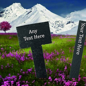 Op de afbeelding: Twee zwarte leisteen tuinmarkeringen met witte tekst. De grotere markering heeft de tekst "Any Text Here" en de kleinere markering heeft de tekst "Your Text Here". De markeringen staan in een veld met paarse bloemen met een besneeuwde bergketen op de achtergrond.