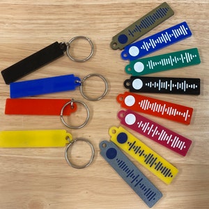 Könnte beinhalten: Zehn bunte Schlüsselanhänger mit unterschiedlich farbigen Balken und einem weißen Barcode-Design. Jeder Schlüsselanhänger hat einen silbernen Ring und einen kleinen Kreis mit einem farbigen Punkt in der Mitte.
