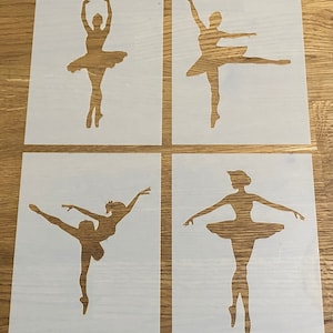 Könnte beinhalten: Vier weiße Schablonen einer Ballerina in verschiedenen Posen. Die Schablonen liegen auf einer Holzoberfläche.