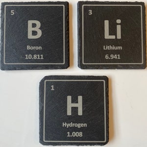 Puede incluir: Tres posavasos cuadrados de pizarra negra con los elementos de la tabla periódica Boro, Litio e Hidrógeno. Cada posavasos muestra el símbolo, el número atómico y el peso atómico del elemento en blanco.
