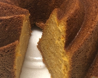Könnte beinhalten: Ein goldbrauner Bundkuchen mit einem herausgenommenen Stück, das das feuchte, hellgelbe Innere zeigt. Der Kuchen liegt auf einem weißen Styroporteller.