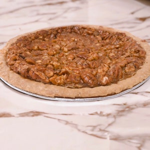 K&ouml;nnte beinhalten: Ein Pecan Pie mit einer goldbraunen Kruste und einer gro&szlig;z&uuml;gigen Menge an Pecann&uuml;ssen auf der Oberseite.