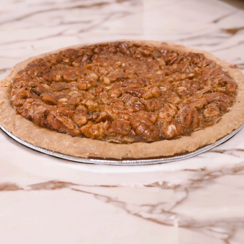 K&ouml;nnte beinhalten: Ein Pecan Pie mit einer goldbraunen Kruste und einer gro&szlig;z&uuml;gigen Menge an Pecann&uuml;ssen auf der Oberseite.