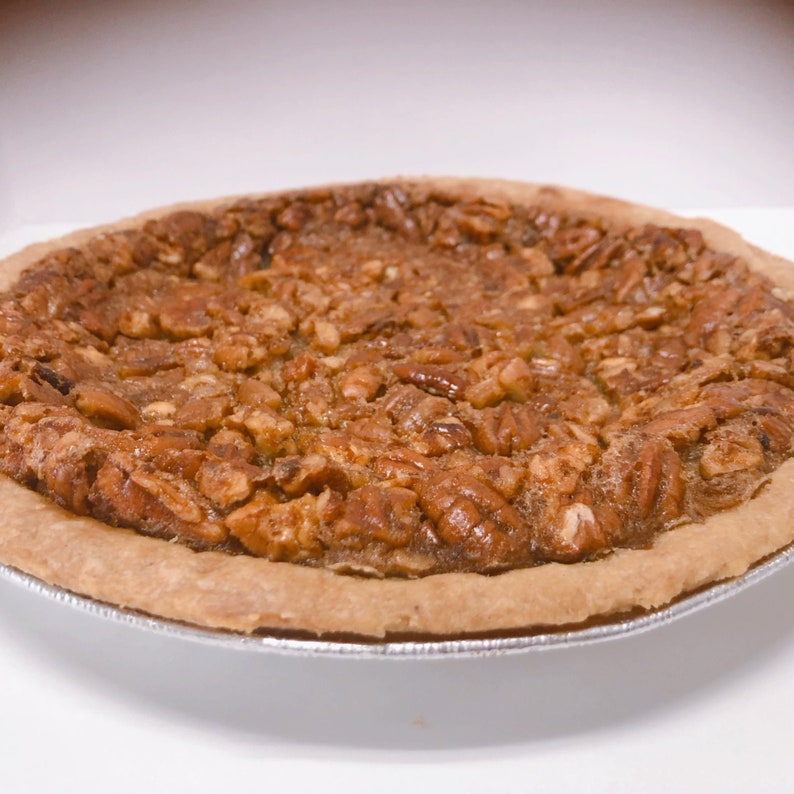 K&ouml;nnte beinhalten: Ein Pecan Pie mit einer goldbraunen Kruste und einer gro&szlig;z&uuml;gigen Schicht Pecann&uuml;sse auf der Oberseite.