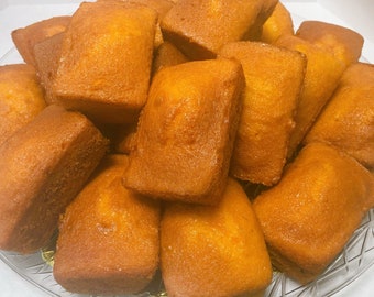 May include: A close-up of a plate of freshly baked, golden brown loaf cakes. The cakes are arranged in a pile, with some overlapping. The cakes have a soft, fluffy texture and a slightly sweet aroma.