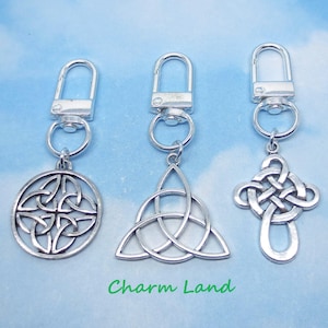 May include: Three silver-toned Celtic knot keychains. The keychains feature a round knot, a triangular knot, and a cross-shaped knot. Each keychain has a clasp for easy attachment. The text "Charm Land" is printed in green.