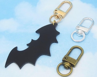 May include: A black bat-shaped charm with a gold-colored clasp, a silver clasp, and a bronze-colored clasp. The charm is attached to a gold-colored clasp. The text "Charm Land" is at the bottom.