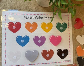 May include: A colorful educational game titled "Heart Color Match" featuring a variety of heart-shaped pieces in different colors. The game includes a matching board with heart outlines and loose heart pieces.