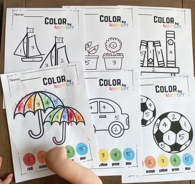 May include: A set of six printable coloring pages with the title "Color by Number". Each page features a different image, including a sailboat, a flower, a bookshelf, an umbrella, a car, and a soccer ball. The images are outlined in black and numbered, and the corresponding colors are listed below each image.