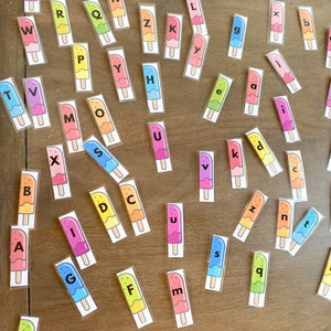 May include: A set of colorful popsicle-shaped letter tiles with the letters of the alphabet printed on them. The tiles are scattered on a wooden surface.