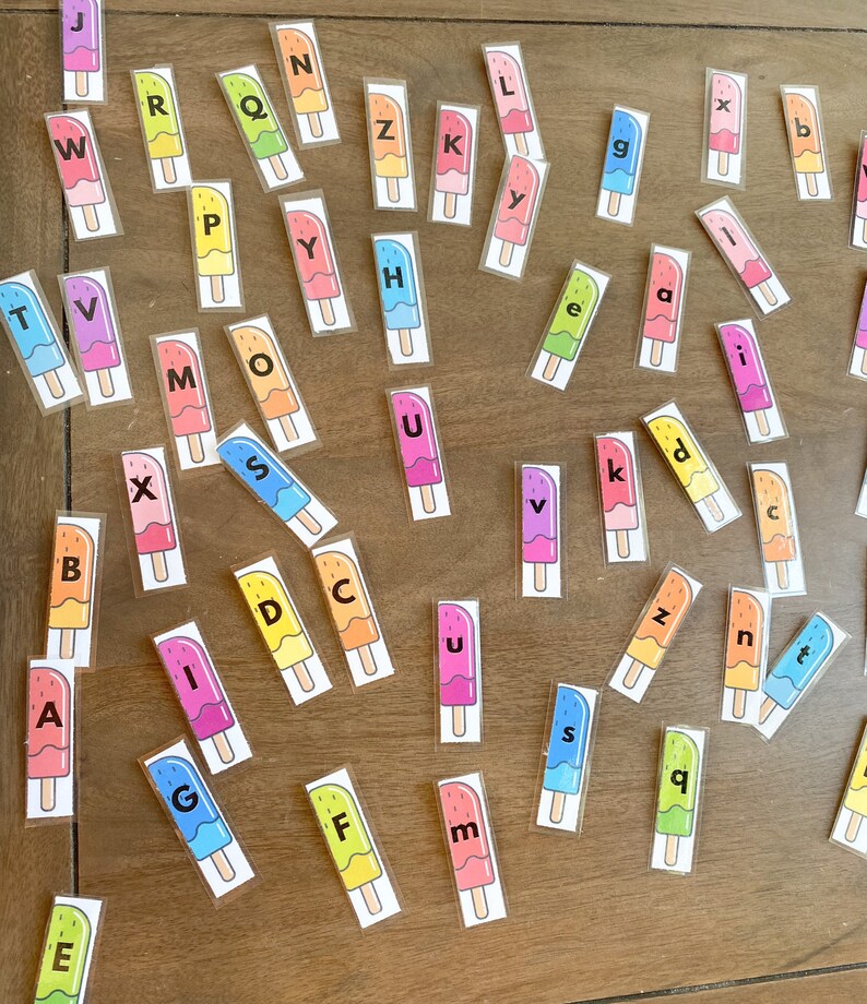 May include: A set of colorful popsicle-shaped letter tiles with the letters of the alphabet printed on them. The tiles are scattered on a wooden surface.